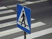 Zdjęcie kolorowe przedstawia znak drogowy ”Przejście dla pieszych” znak jest kwadratowy w niebieskim kolorze w środku znaku znajduje się biały trójkąt w którym umieszczony jest ludzik w czarnym kolorze