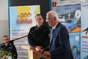 prezydent miasta Krosna, przedstawiciel straży pożarnej i policji podczas spotkania z seniorami. W tle banery promujące szkołę, na terenie której zorganizowano spotkanie