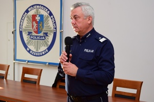 Policjanci podczas spotkania z uczniami. Policjanci stoją, uczniowie siedzą przy długich stołach.