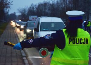 Policjantka zatrzymuje do kontroli samochód. W rękach trzyma tarczę do zatrzymywania i urządzenie do sprawdzania trzeźwości