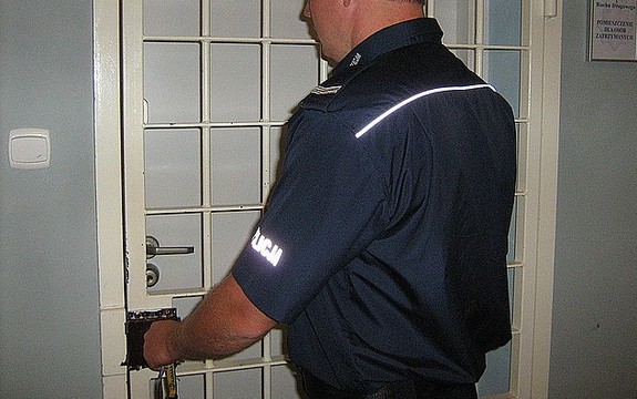 Na zdjęciu policjant, który zamyka  pomieszczenie dla osób zatrzymanych.