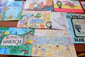 Policjanci i zaproszeni członkowie jury przeglądają prace konkursowe rozłożone na stołach.