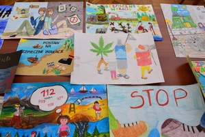 Policjanci i zaproszeni członkowie jury przeglądają prace konkursowe rozłożone na stołach.