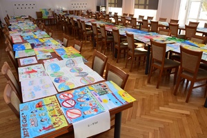 Policjanci i zaproszeni członkowie jury przeglądają prace konkursowe rozłożone na stołach.