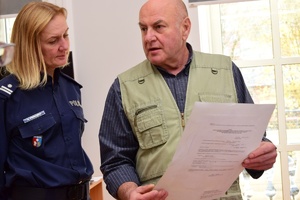 Policjanci i zaproszeni członkowie jury przeglądają prace konkursowe rozłożone na stołach.