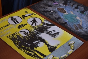 Policjanci i zaproszeni członkowie jury przeglądają prace konkursowe rozłożone na stołach.