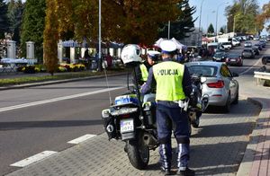 Policjanci przy motocyklach. W tle droga oraz cmentarz