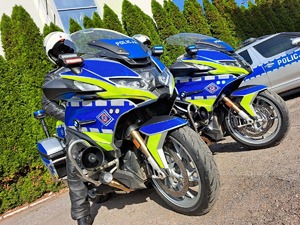 na fotografii dwa nowe policyjne motocykle, na jednym z nich siedzi policjant, w tle widać radiowóz