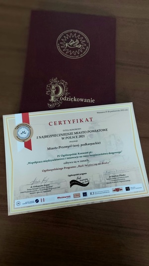 zdjęcie przedstawia Certyfikat dla Miasta Przemyśl przyznający  honorowy tytuł „I Najbezpieczniejsze Miasto Powiatowe w Polsce 2021” wraz z pamiątkową statuetką, oraz dyplom za podejmowanie wysiłków w działaniu na rzecz poprawy bezpieczeństwa na drogach