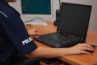 Umundurowany policjant siedzący przy biurku, na którym znajduje się komputer.