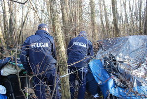 Dwóch policjantów sprawdzających miejscach gdzie mogą przebywać osoby bezdomne, w tle drzewa