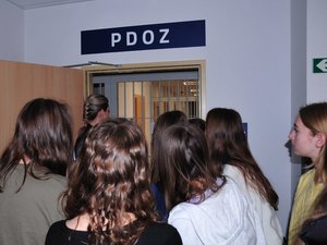 grupa uczniów spogląda przez otwarte drzwi na kraty w pomieszczeniach dla osób zatrzymanych