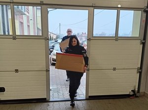 Funkcjonariuszka wchodząc do budynki hospicjum wnosi pudełko