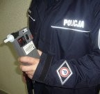 Umundurowany policjant trzymający w ręce urządzenie do badania stanu trzeźwości.