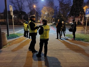 Na zdjęciu na  pierwszym planie policjanci ruchu drogowego w żółtych kamizelkach odblaskowych z napisem policja na plecach. W dalszym tle tuz przed przejściem dla pieszych przedstawiciele Wojewódzkiego Ośrodka Ruchu Drogowego, Strzelców oraz prasy.