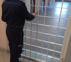 Umundurowany policjant zamykający drzwi prowadzące do aresztu.