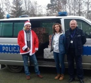 Policjant wraz z pracownikami Miejskiego Ośrodka Pomocy Społecznej przy radiowozie z paczkami świątecznymi