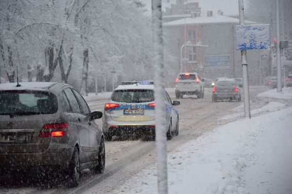 na zdjęciu zaśnieżona droga oraz jadące samochody w tym policyjny radiowóz