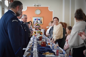 Policjanci podczas spotkania z rodzinami poległych policjantów. Uczestnicy spotkania dzielą się opłatkiem i składają sobie życzenia przy wigilijnym stole.