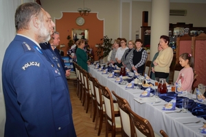 Policjanci podczas spotkania z rodzinami poległych policjantów. Uczestnicy spotkania dzielą się opłatkiem i składają sobie życzenia przy wigilijnym stole.