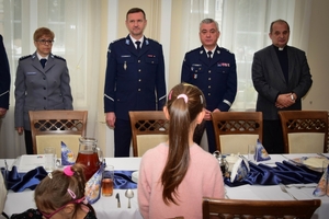 Policjanci podczas spotkania z rodzinami poległych policjantów. Uczestnicy spotkania dzielą się opłatkiem i składają sobie życzenia przy wigilijnym stole.