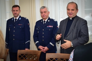 Policjanci podczas spotkania z rodzinami poległych policjantów. Uczestnicy spotkania dzielą się opłatkiem i składają sobie życzenia przy wigilijnym stole.