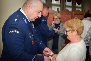 Policjanci podczas spotkania z rodzinami poległych policjantów. Uczestnicy spotkania dzielą się opłatkiem i składają sobie życzenia przy wigilijnym stole.