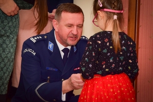 Policjanci podczas spotkania z rodzinami poległych policjantów. Uczestnicy spotkania dzielą się opłatkiem i składają sobie życzenia przy wigilijnym stole.