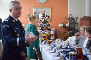 Policjanci podczas spotkania z rodzinami poległych policjantów. Uczestnicy spotkania dzielą się opłatkiem i składają sobie życzenia przy wigilijnym stole.