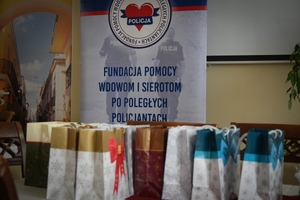 Policjanci podczas spotkania z rodzinami poległych policjantów. Uczestnicy spotkania dzielą się opłatkiem i składają sobie życzenia przy wigilijnym stole.