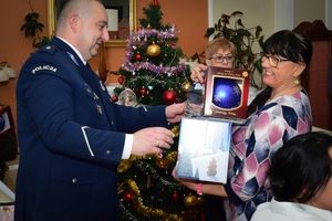 Policjanci podczas spotkania z rodzinami poległych policjantów. Uczestnicy spotkania dzielą się opłatkiem i składają sobie życzenia przy wigilijnym stole.