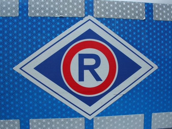 odblaskowa naklejka na bocznych drzwiach radiowozu - litera R w czerwonym okręgu oznaczająca rodzaj służby tj. wydział ruchu drogowego