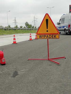 znak uwaga niebezpieczeństwo oraz czerwona lampa oznaczające miejsce wypadku, w tle radiowóz