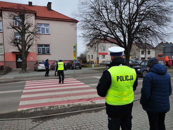 na zdjęciu oznakowane przejście dla pieszych w kolorach biało czerwonych oraz po obu stronach przejścia umundurowani policjanci