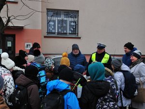 na zdjęciu grupa dzieci w rejonie przejścia dla pieszych zwrócona przodem do policjanta oraz członków komisji alkoholowej