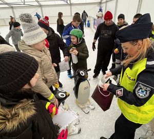 Fotografia przedstawia umundurowane policjantki w kamizelkach odblaskowych prowadzące rozmowę z dziećmi na temat bezpieczeństwa podczas ferii zimowych