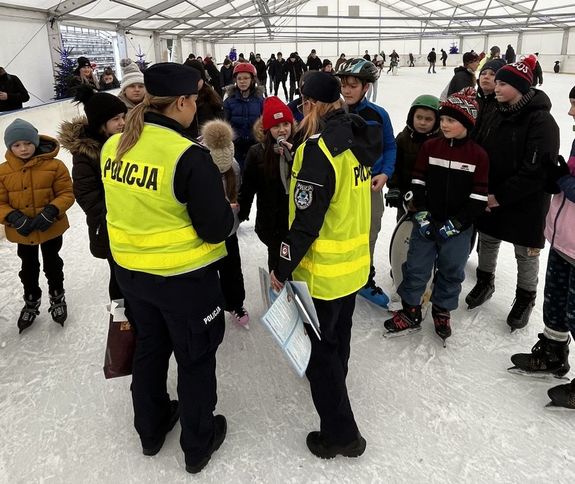 Fotografia przedstawia umundurowane policjantki w kamizelkach odblaskowych prowadzące rozmowę z dziećmi na temat bezpieczeństwa podczas ferii zimowych