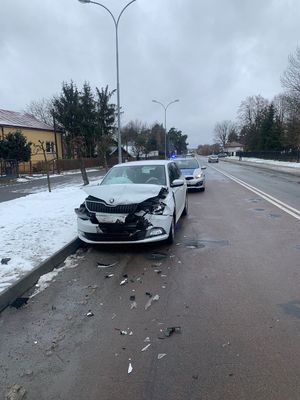Rozbity po kolizji samochód koloru białego a za nim policyjny radiowóz.