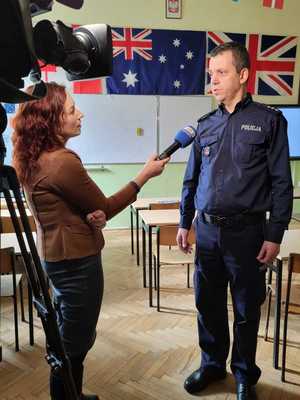 Funkcjonariusz rozmawiający z dziennikarką, w klasie szkolnej