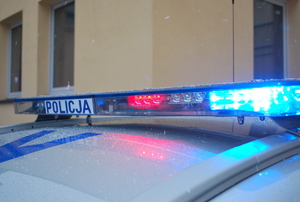 Na zdjęciu belka policyjnego radiowozu z napisem policja oraz włączonymi światłami uprzywilejowania.