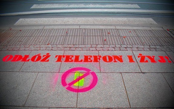 zdjęcie przedstawia fragment przejścia dla pieszych z napisem w kolorze czerwonym &quot;odłóż telefon i żyj&quot;