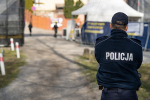 Zdjęcie przedstawia policjanta stojącego tyłem. Na plecach ma napis &quot;Policja&quot;. Zdjęcie z zabezpieczenia przyjazdu pielgrzymów chasydzkich do Leżajska.
