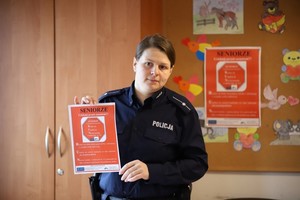 Policjantka prezentuje plakat promujący kampanię „Seniorze ucieknij przed oszustem”