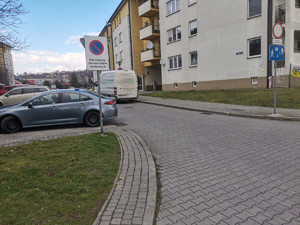 zdjęcie przedstawia teren przy ul. Równej w Przemyślu gdzie doszło do zdarzenia. na zdjęciu widoczny jest blok, oraz parking gdzie zaparkowane są samochody. na pierwszym planie widoczny jest biały bus i nieoznakowany radiowóz policyjny.