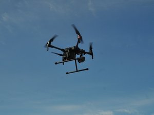 Na zdjęciu widoczny jest policyjny dron unoszący się w powietrzu.