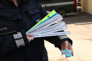 Na zdjęciu umundurowana policjantka pokazuje opaski i breloczki odblaskowe.
