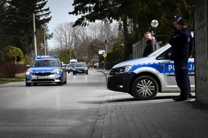 Policjanci podczas zabezpieczenia obchodów 79. rocznicy śmierci Rodziny Ulmów. Po prawej stojący radiowóz, na pierwszym planie jadący radiowóz a za nim kolumna pojazdów prezydenckich.