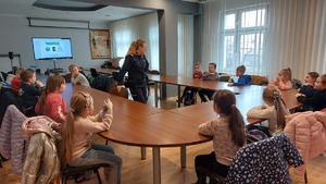 zdjęcia przedstawiają dzieci z klasy pierwszej na spotkaniu z policjantką w Komendzie Miejskiej Policji w Przemyślu. Uczniowie siedzą na auli przy stolikach i słuchają prelekcji policjantki.
