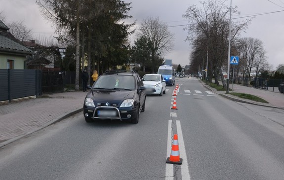 Ustawione na ulicy Bursaki w Krośnie kolejno renault, ford oraz policyjny radiowóz z włączonymi sygnałami świetlnymi w kolorze niebieskim. Przy osi jezdni pachołki drogowe