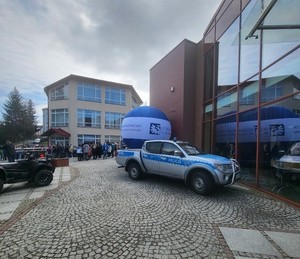 Policyjny radiowóz prezentowany podczas „Dnia otwartego” uczelni. W tle balon reklamujący sanocką uczelnię oraz inne stoiska informacyjne